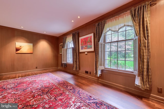 spare room with wood walls, wood-type flooring, and ornamental molding