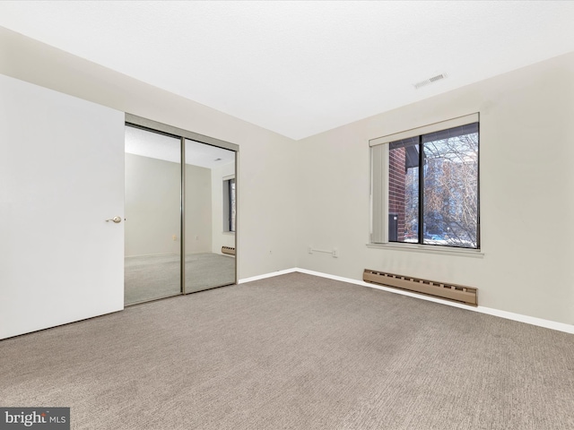 unfurnished bedroom with carpet, a closet, and a baseboard heating unit