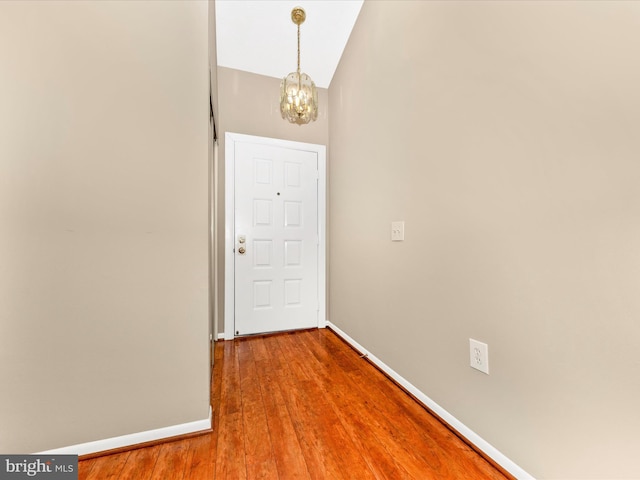 hallway with hardwood / wood-style floors, a chandelier, and vaulted ceiling