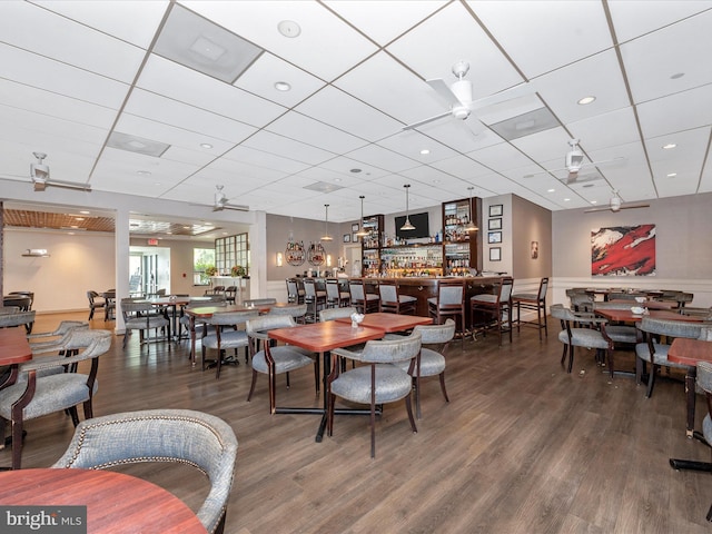 dining space featuring bar area, hardwood / wood-style floors, a drop ceiling, and ceiling fan