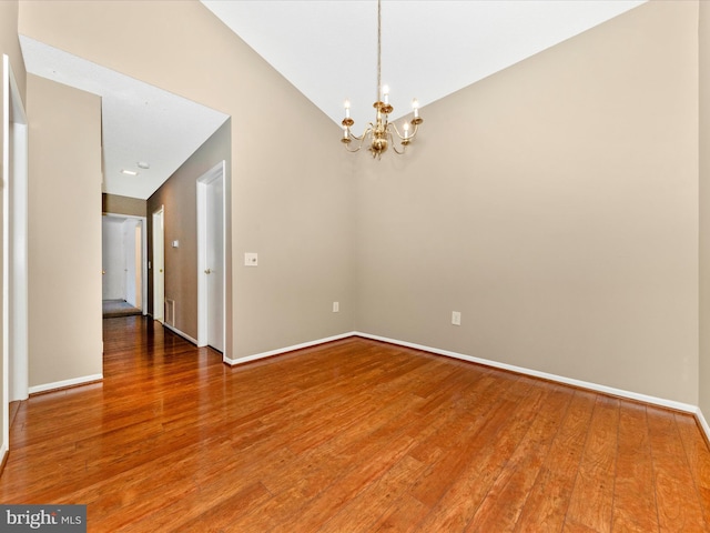 empty room featuring wood-type flooring, vaulted ceiling, and an inviting chandelier