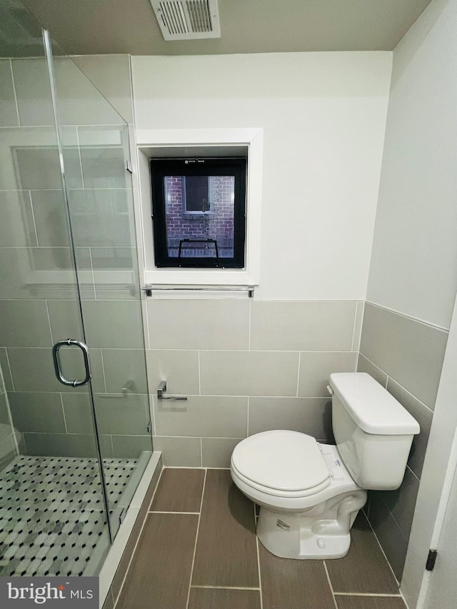 bathroom with walk in shower, tile patterned floors, toilet, and tile walls