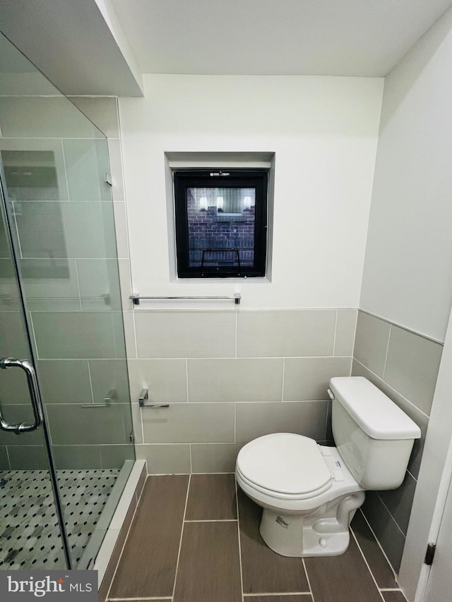 bathroom with tile patterned floors, toilet, tile walls, and a shower with shower door