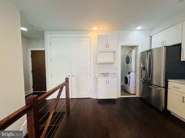 kitchen featuring white cabinets, dark hardwood / wood-style floors, stainless steel fridge, stacked washer / drying machine, and light stone counters