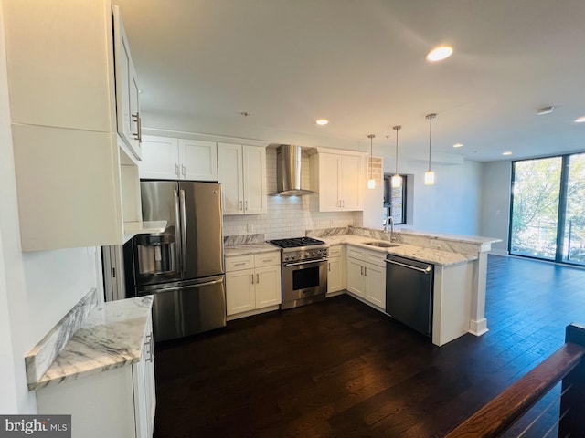 kitchen featuring pendant lighting, wall chimney range hood, dark hardwood / wood-style floors, kitchen peninsula, and stainless steel appliances