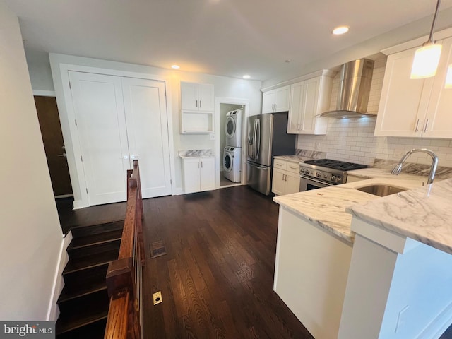 kitchen with white cabinetry, sink, stainless steel appliances, wall chimney range hood, and stacked washer / dryer