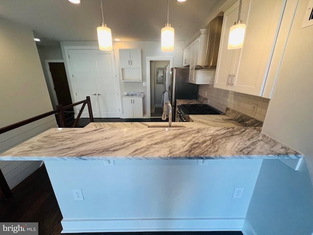 kitchen with white cabinets, wall chimney range hood, decorative light fixtures, light stone counters, and kitchen peninsula