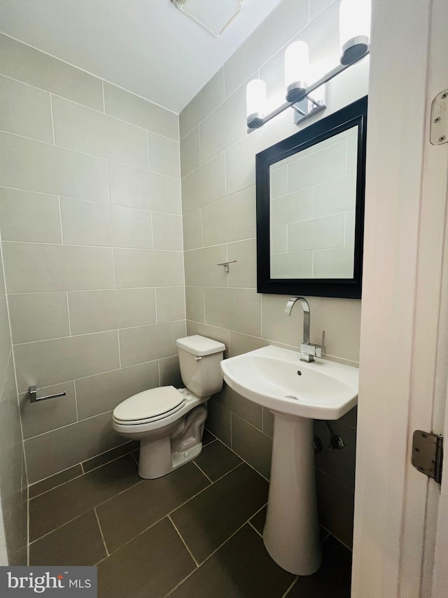 bathroom with tile patterned flooring, toilet, and tile walls