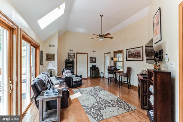 living room featuring ceiling fan, light hardwood / wood-style floors, high vaulted ceiling, and a skylight