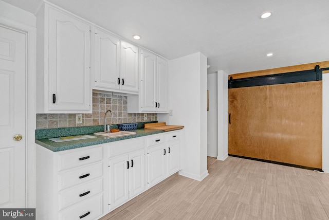 kitchen with tasteful backsplash, sink, a barn door, white cabinets, and light hardwood / wood-style floors