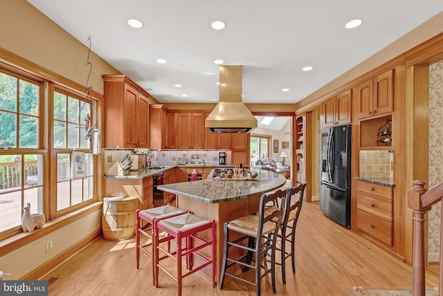 kitchen with a healthy amount of sunlight, backsplash, island range hood, and black appliances