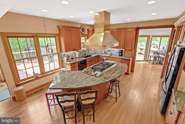 kitchen with a center island, hanging light fixtures, light hardwood / wood-style flooring, decorative backsplash, and light stone counters