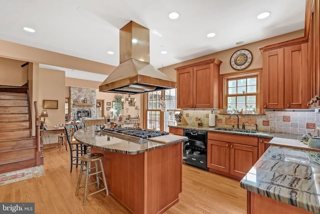 kitchen featuring dishwasher, a center island, light hardwood / wood-style floors, island exhaust hood, and stainless steel gas cooktop