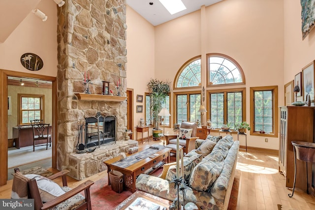 living room with light wood-type flooring, high vaulted ceiling, a wealth of natural light, and a stone fireplace