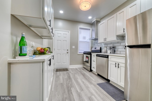 kitchen with white cabinets, wall chimney exhaust hood, decorative backsplash, light wood-type flooring, and appliances with stainless steel finishes