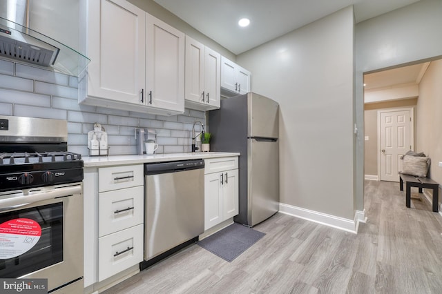 kitchen with wall chimney exhaust hood, decorative backsplash, appliances with stainless steel finishes, light hardwood / wood-style floors, and white cabinetry