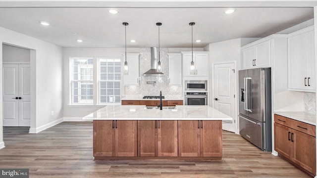 kitchen featuring pendant lighting, wall chimney range hood, an island with sink, white cabinetry, and stainless steel appliances