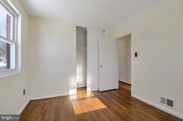 unfurnished bedroom with a closet, dark hardwood / wood-style floors, and multiple windows