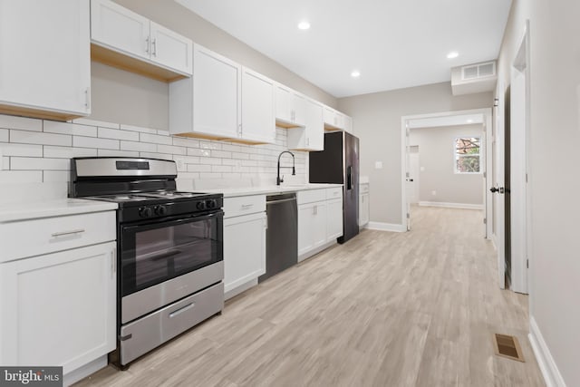 kitchen with appliances with stainless steel finishes, light wood-type flooring, white cabinetry, and sink