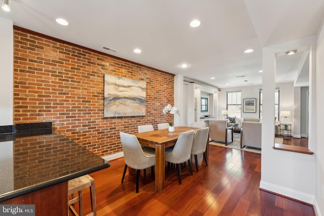 dining space with brick wall and dark hardwood / wood-style flooring