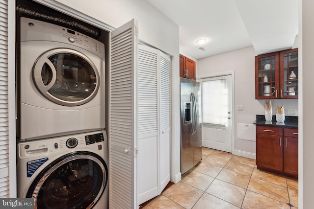 laundry area with stacked washer and clothes dryer and light tile patterned floors