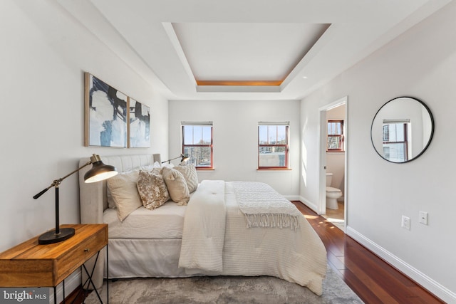 bedroom featuring ensuite bathroom, dark wood-type flooring, and a tray ceiling