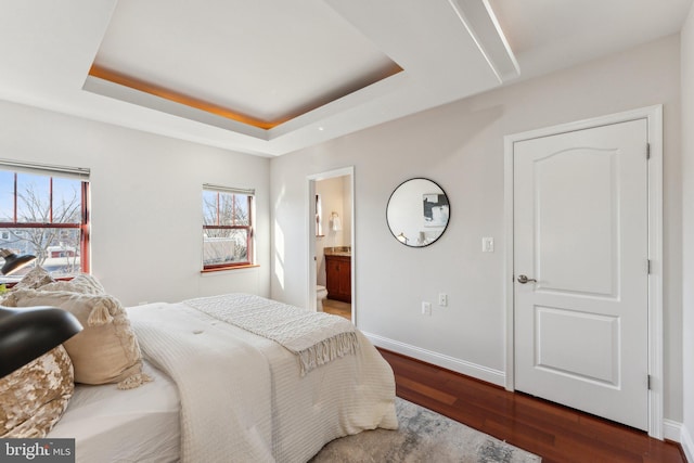 bedroom featuring dark wood-type flooring, a raised ceiling, and ensuite bathroom