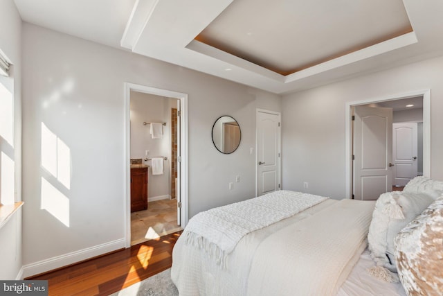 bedroom featuring connected bathroom, a tray ceiling, and light wood-type flooring