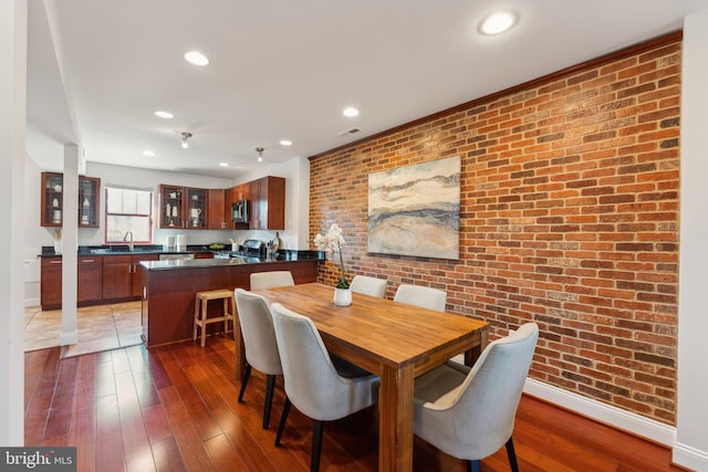 dining room with dark hardwood / wood-style flooring, sink, and brick wall