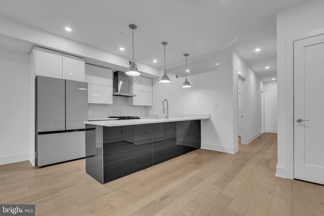 kitchen featuring a breakfast bar, white cabinets, wall chimney exhaust hood, stainless steel fridge, and decorative light fixtures