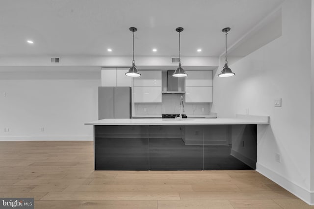 kitchen featuring stainless steel refrigerator, white cabinetry, wall chimney exhaust hood, hanging light fixtures, and light hardwood / wood-style flooring