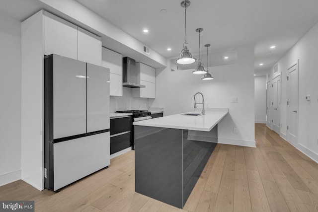 kitchen featuring wall chimney range hood, white cabinetry, sink, and fridge