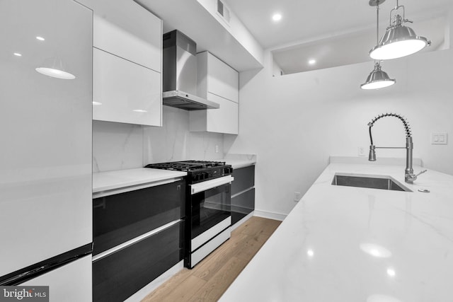 kitchen with wall chimney exhaust hood, sink, white cabinets, and gas range oven