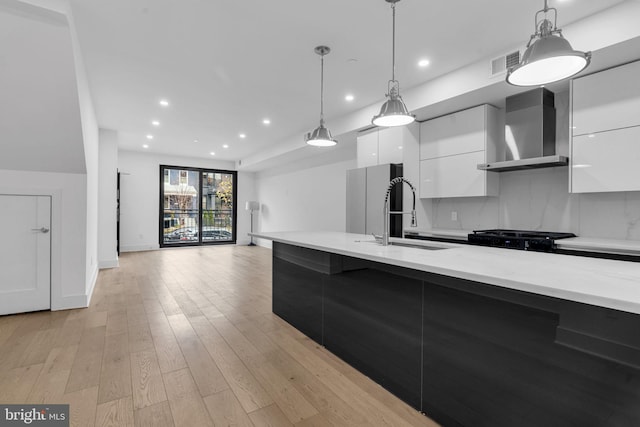 kitchen featuring white cabinets, pendant lighting, light wood-type flooring, and wall chimney exhaust hood