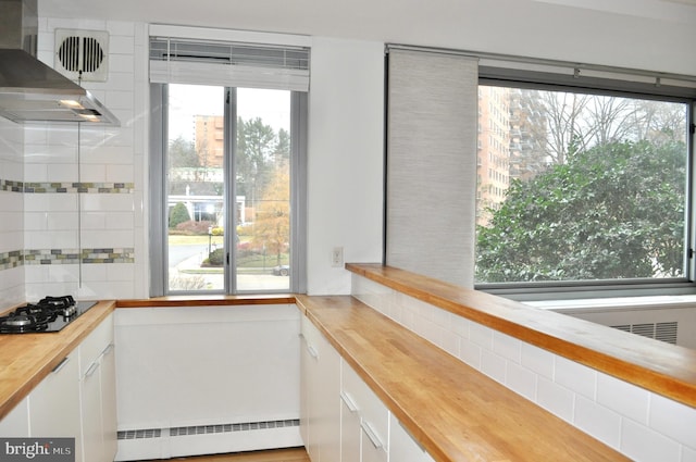 interior space with a baseboard heating unit, white cabinets, wall chimney range hood, and wood counters