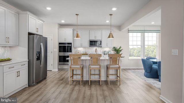 kitchen featuring white cabinets, pendant lighting, an island with sink, and appliances with stainless steel finishes