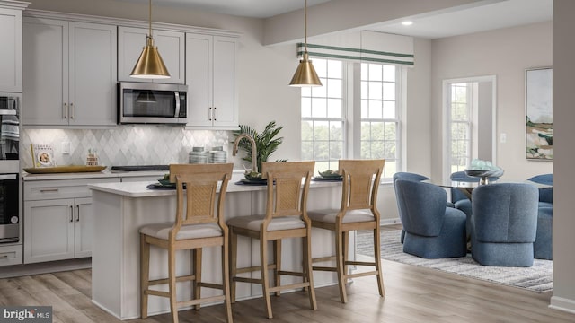 kitchen featuring stainless steel appliances, light hardwood / wood-style flooring, decorative light fixtures, a breakfast bar area, and decorative backsplash