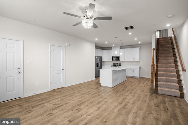 kitchen featuring appliances with stainless steel finishes, ceiling fan, a kitchen island with sink, white cabinets, and hanging light fixtures