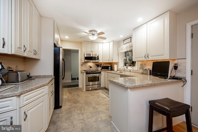 kitchen with stainless steel appliances, light stone counters, kitchen peninsula, decorative backsplash, and white cabinets