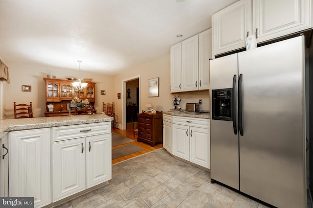 kitchen featuring white cabinets, stainless steel refrigerator with ice dispenser, hanging light fixtures, light stone counters, and a chandelier