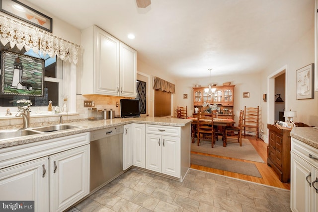 kitchen featuring kitchen peninsula, stainless steel dishwasher, sink, decorative light fixtures, and white cabinetry