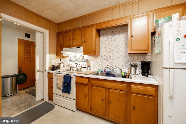 kitchen featuring white appliances, wood walls, and sink