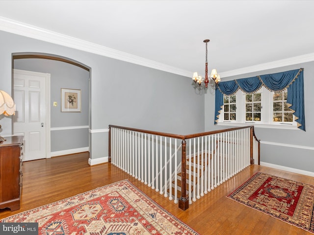 hall with hardwood / wood-style flooring, ornamental molding, and a notable chandelier