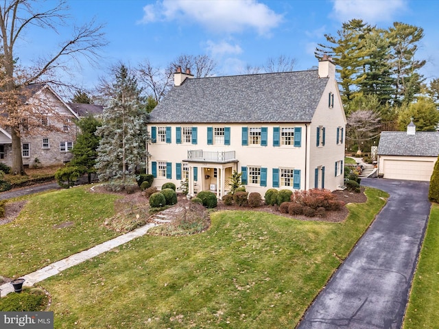 colonial inspired home featuring a garage, a balcony, an outbuilding, and a front lawn