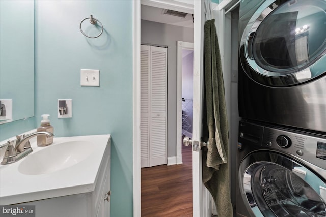 clothes washing area with stacked washing maching and dryer, dark hardwood / wood-style floors, and sink