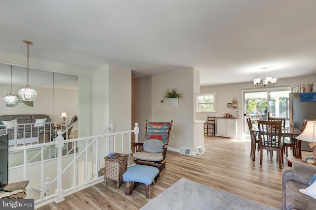living area featuring visible vents, wood finished floors, a chandelier, and baseboards