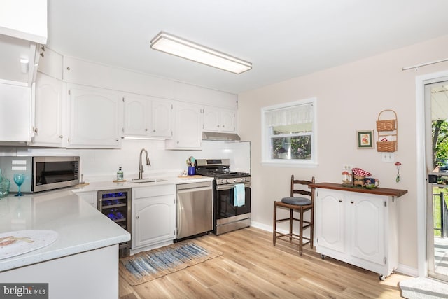 kitchen featuring a sink, under cabinet range hood, white cabinets, appliances with stainless steel finishes, and beverage cooler