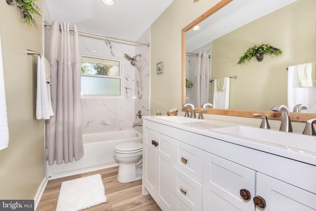 full bathroom featuring wood finished floors, double vanity, shower / bath combo with shower curtain, toilet, and a sink