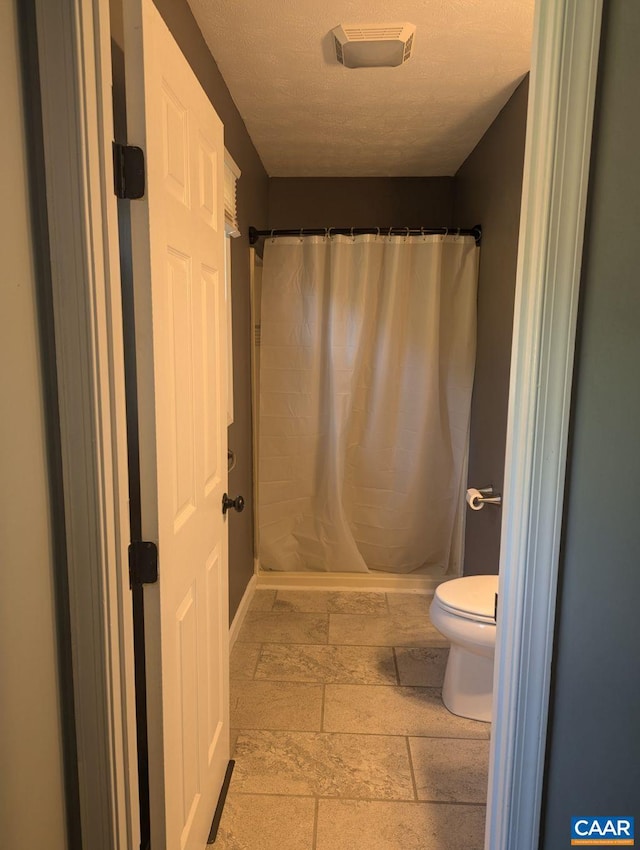 bathroom featuring curtained shower, a textured ceiling, and toilet