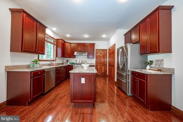 kitchen with a kitchen island, light stone countertops, appliances with stainless steel finishes, and dark wood-type flooring